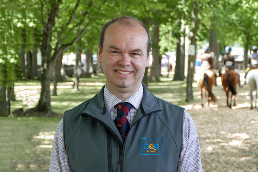 Man standing in foreground with trees and horses in background