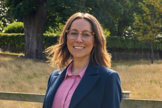 Lady in blue jacket and pink blouse in front of a field and tree